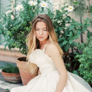 A beautiful bride in a wedding dress sitting gracefully in a garden with daisies.
